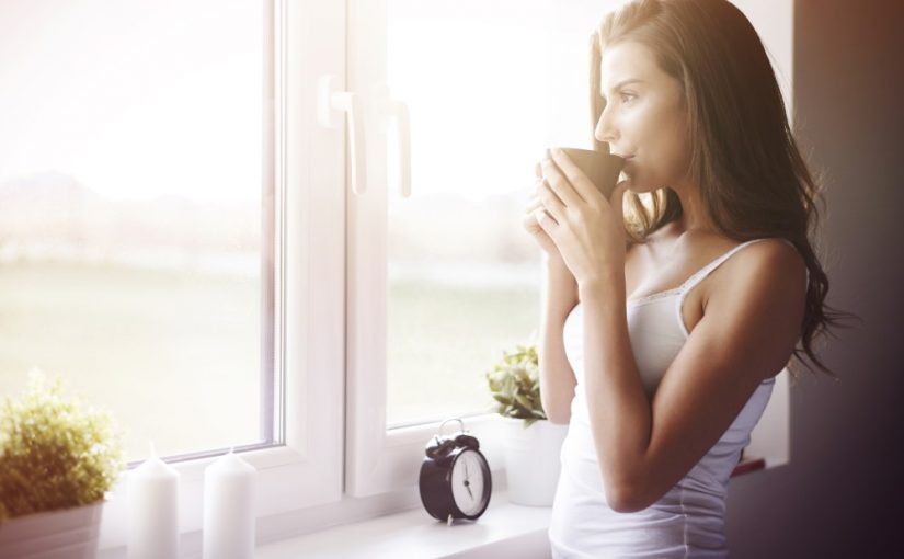 Kvinde der drikker kaffe og kigger ud af vinduet